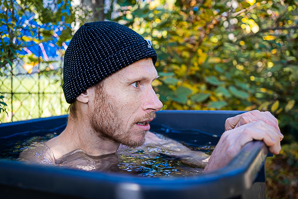 Ein Mann sitzt in einem Becken mit Wasser beim Eisbaden. Er trägt dabei eine Mütze