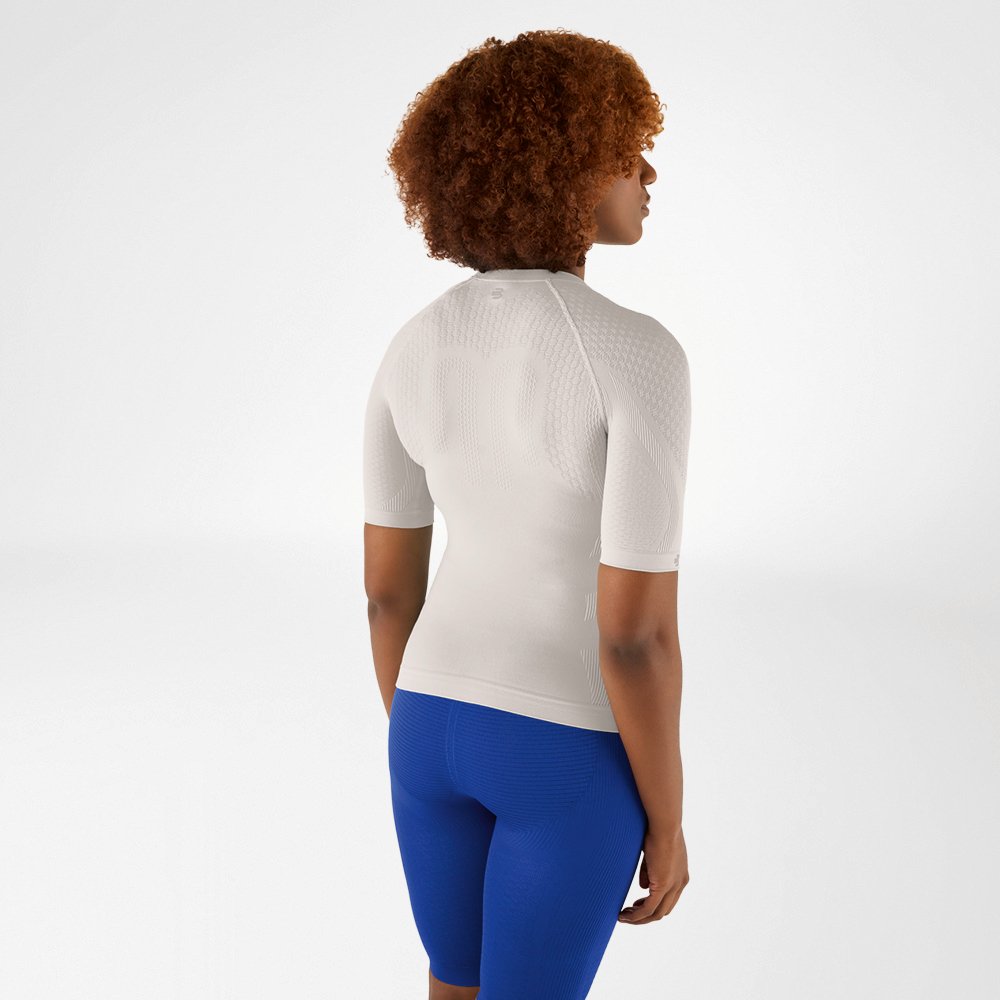 Back view of a woman with curly hair in a silver-grey compression shirt and blue leggings, looking slightly to the side.