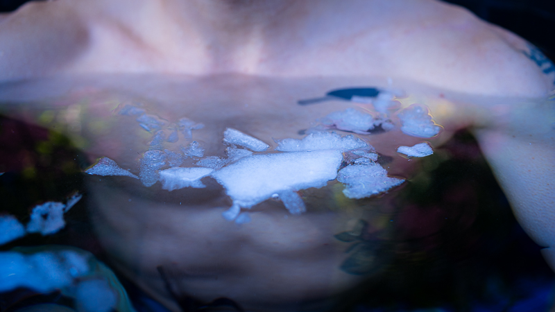 Close-up of a person’s upper body during ice bathing, ice chunks floating on the water surface in front of the chest.