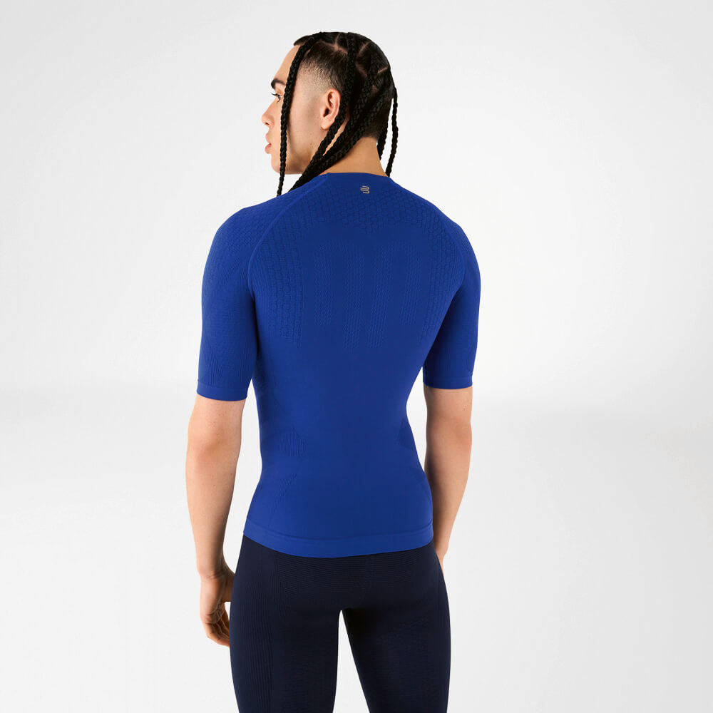 A man wearing a blue compression shirt stands with his back to the camera, looking over his shoulder.