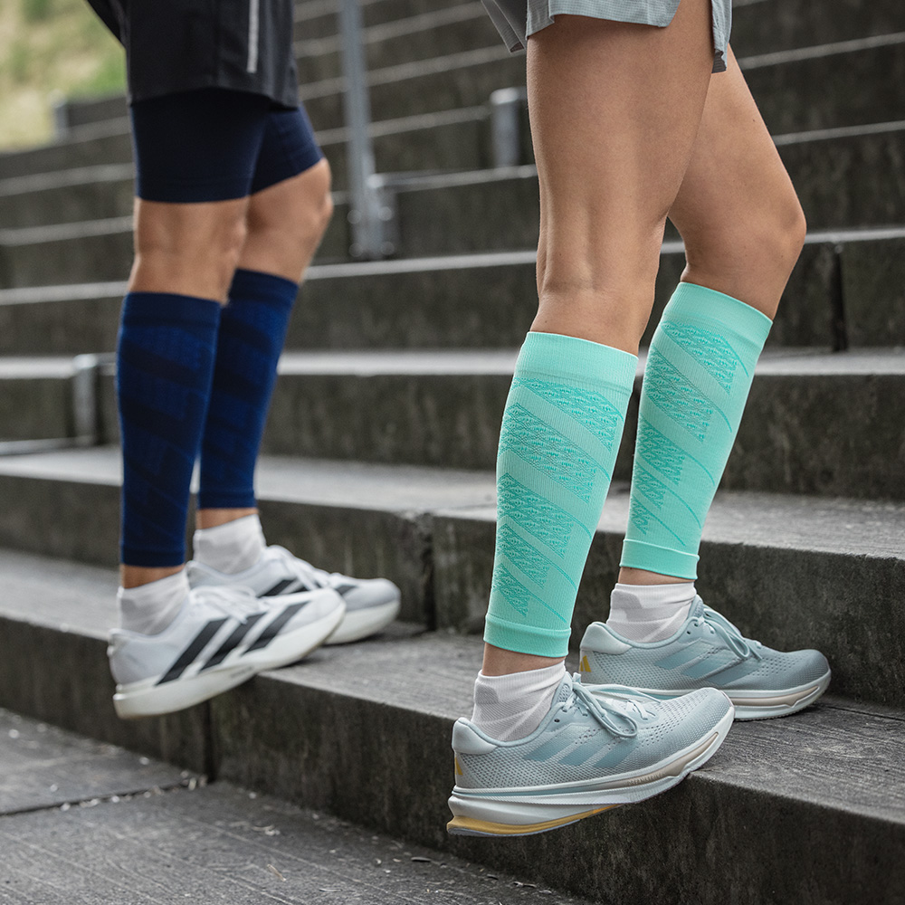 Two runners training on outdoor stairs. They wear Run Performance Sleeves with compression in mint and navy, supporting calf stability and improving circulation.