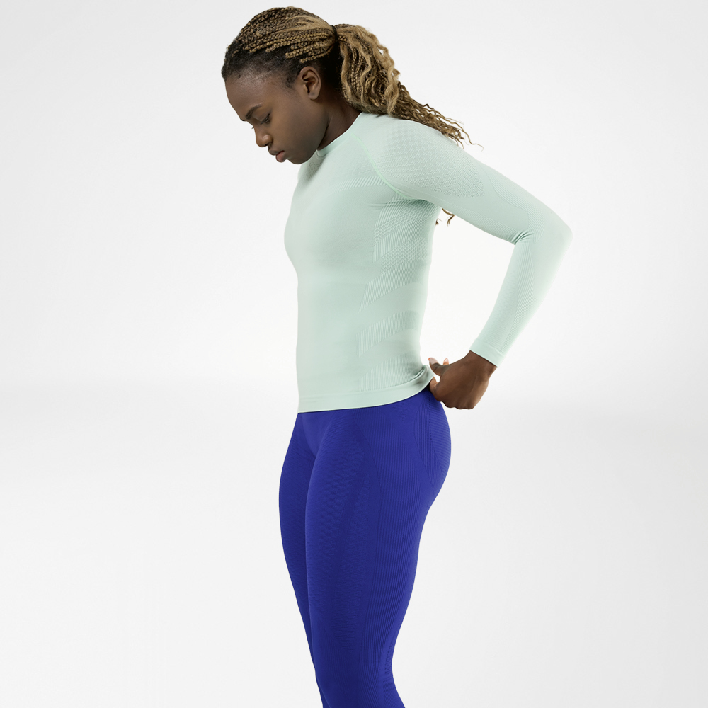 Woman in a mint green long sleeve shirt and blue compression pants, side view