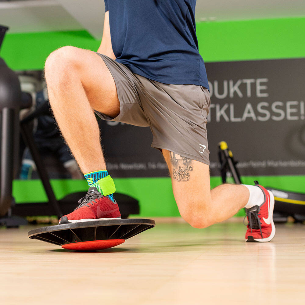 Man in a gym makes a lung with the front leg standing on a balance pad and wearing an ankle bandage