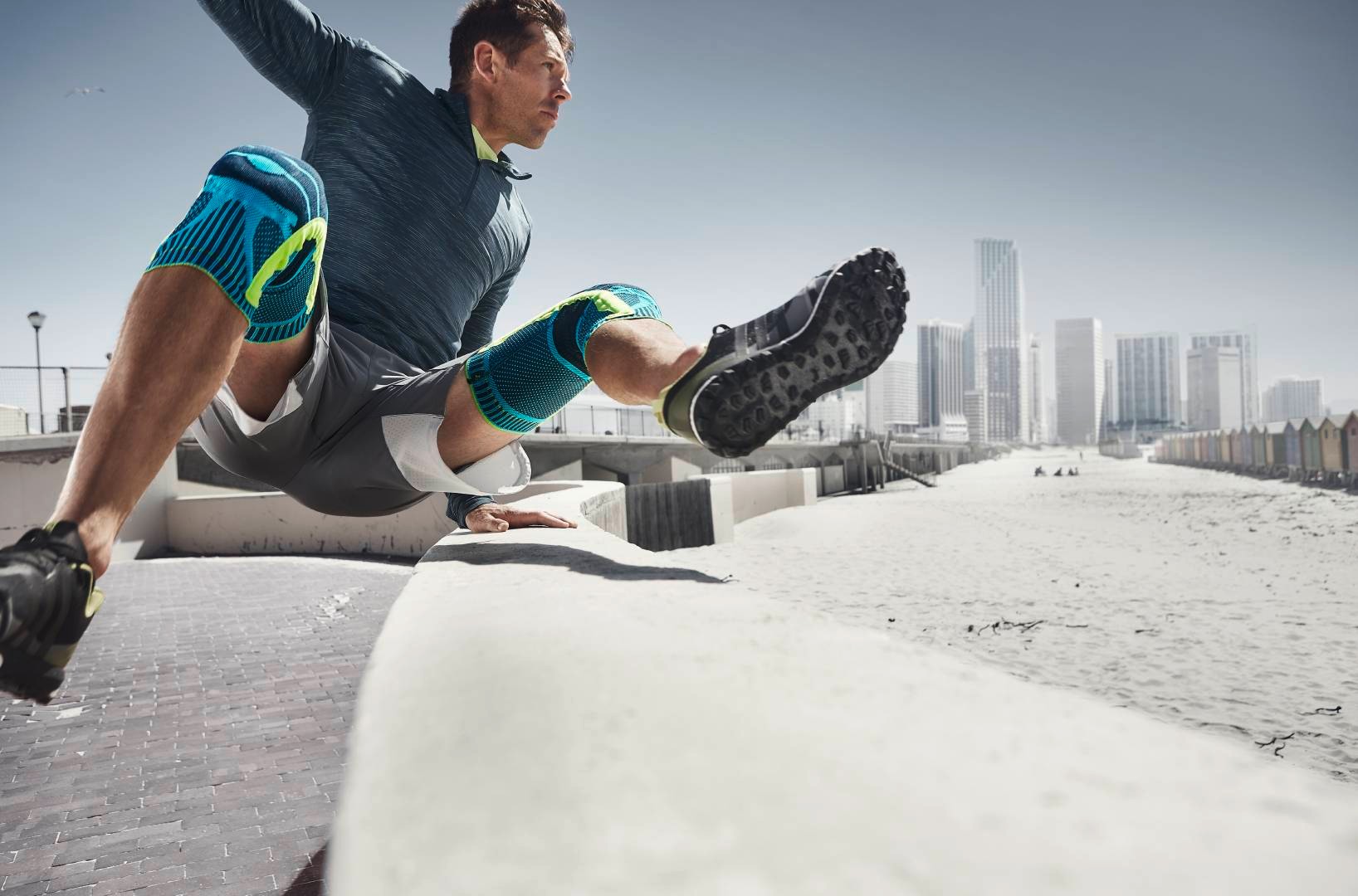 Mann with two knee bands jumps over an obstacle in the background of the Urban Running