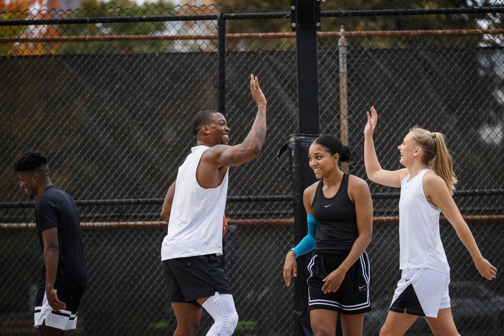 Two basketball players in white game clothes clap cheerfully while their opponents in black look into different directions in black