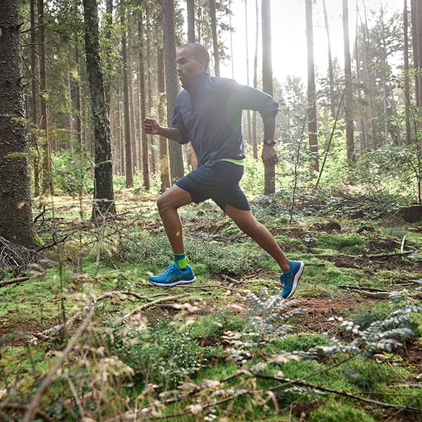 A man is running through a dense forest wearing an Achilles bandage.