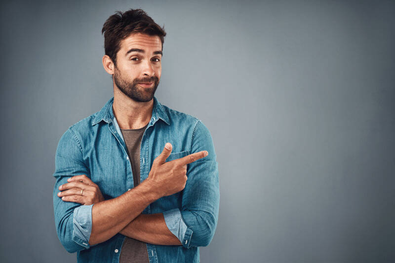 Smiling man in a denim shirt shows with his index finger to the side