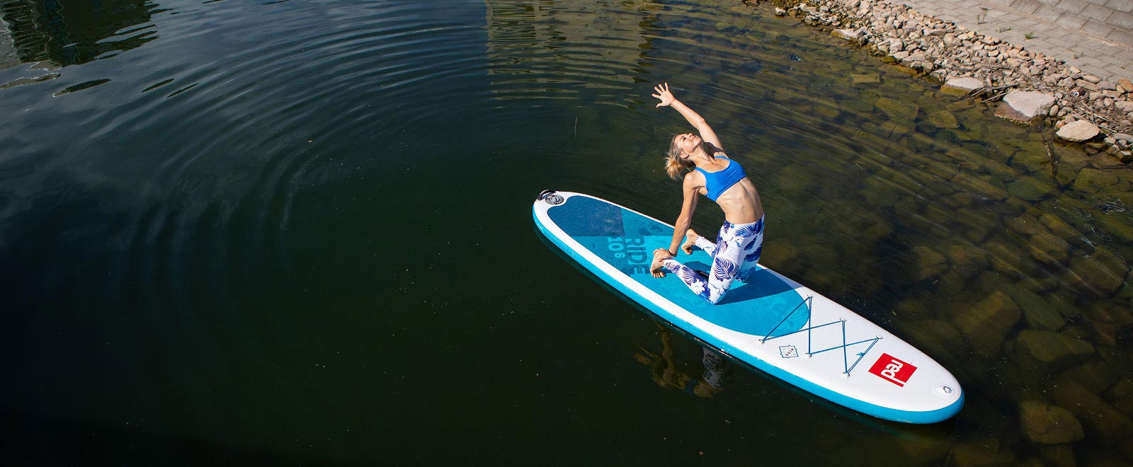Woman makes yoga exercise on SUP board near the shore under water a few stones are visible