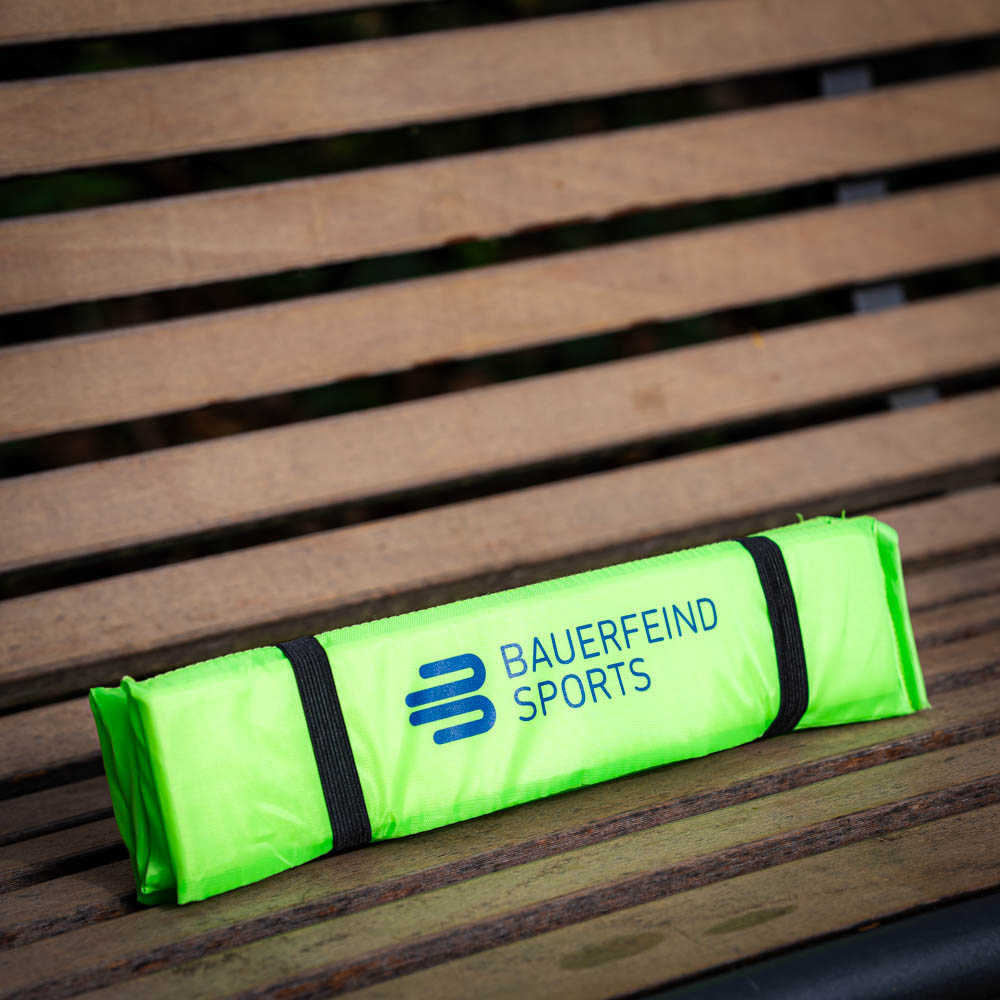 Folded Bauerfeind Sports seat cushion in bright green, securely stored on a wooden bench.
