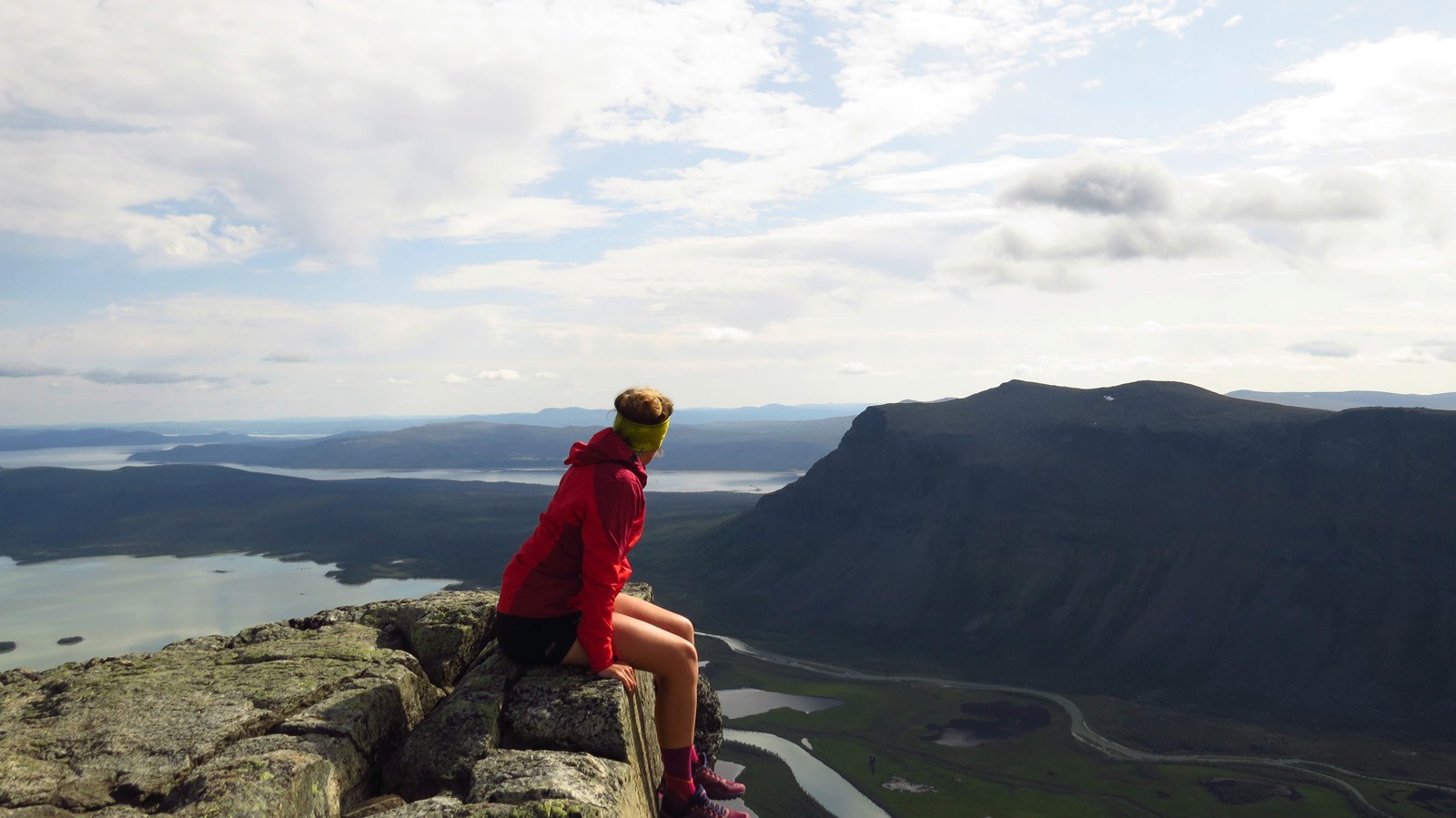 Frau sits on a rocky lead and looks into the distance towards mountains and lakes