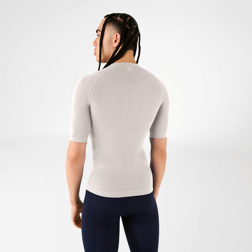 A man wearing a silver-grey compression shirt stands with his back to the camera, looking over his shoulder.