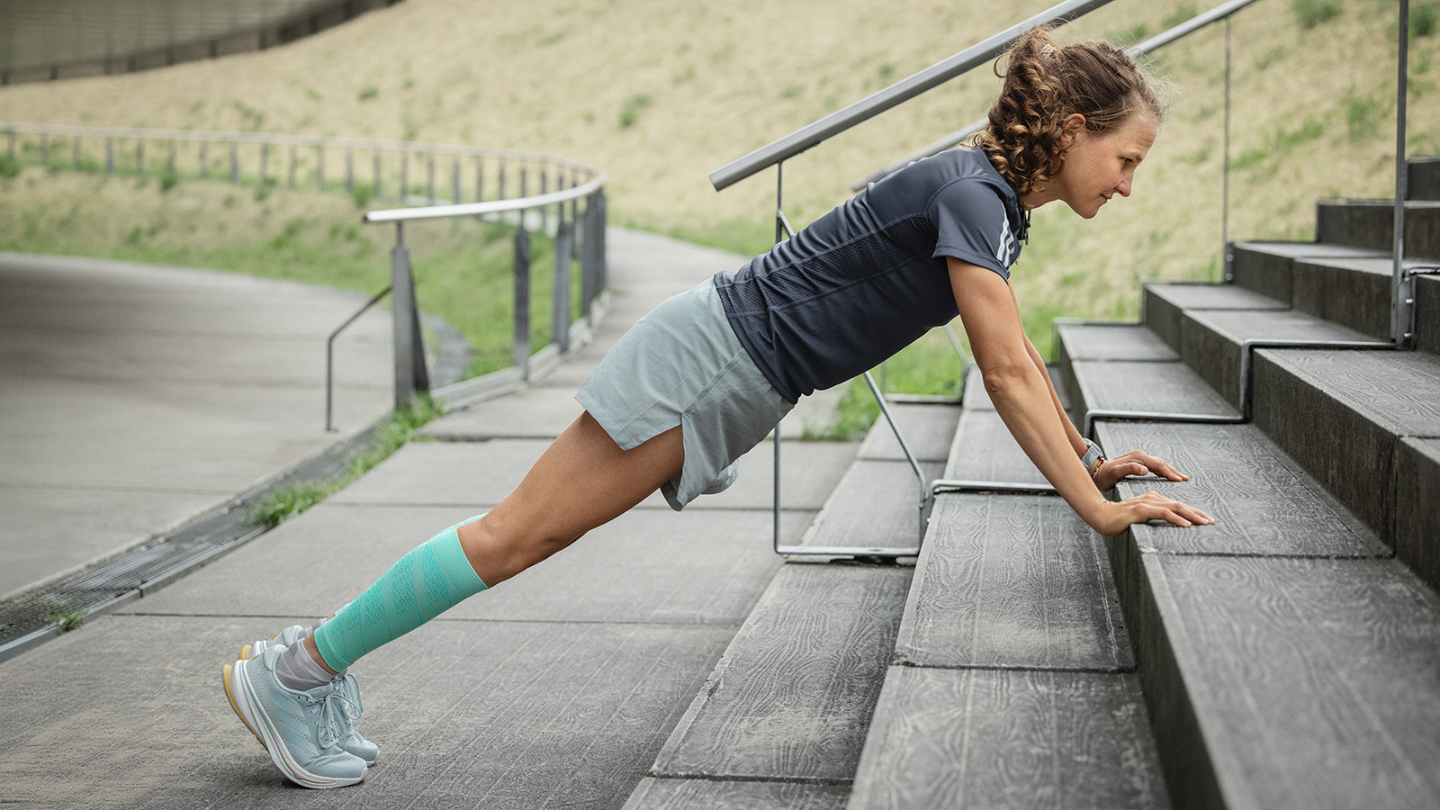 Woman makes push-ups on a concrete floor in the background a man stretches on a wall