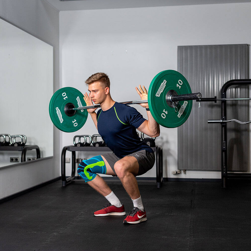 Man in the gym with a knee tandage makes a squat with a barbell on the back