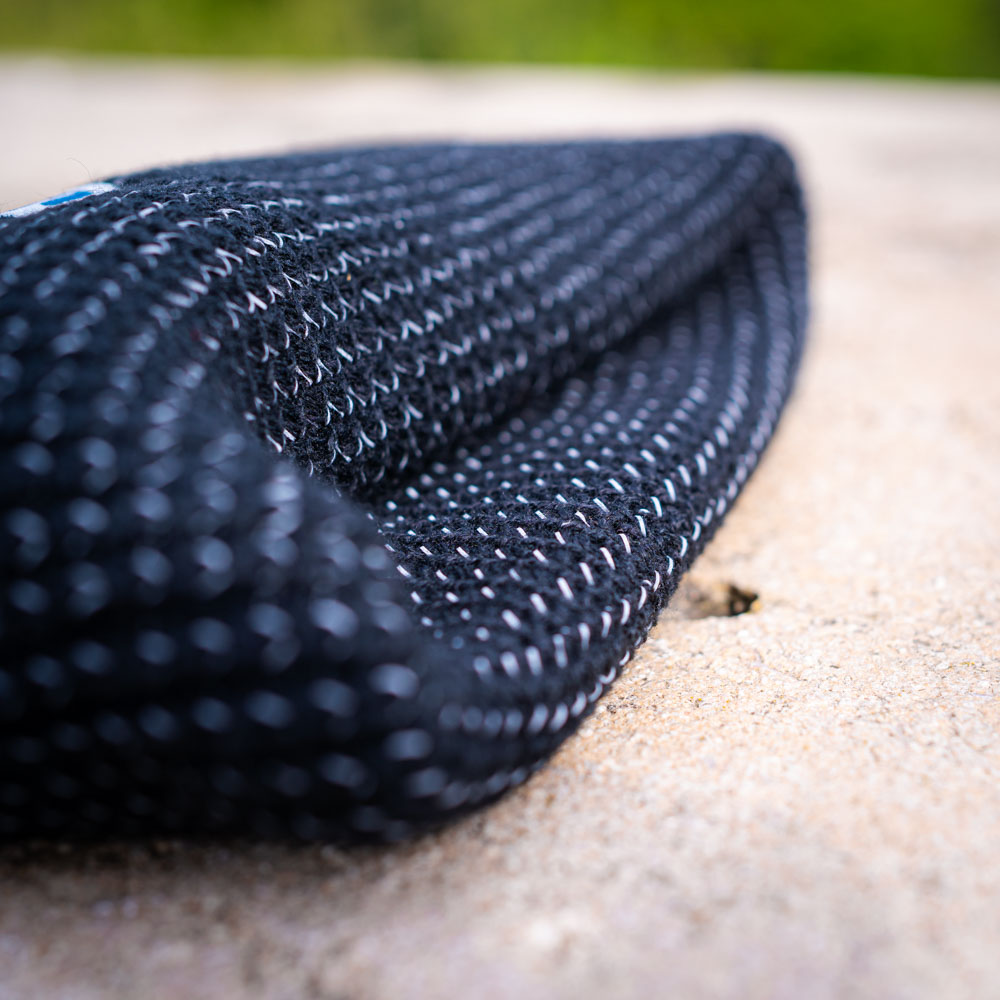 A folded black Bauerfeind Sports beanie on a rock, with the chunky texture clearly visible.