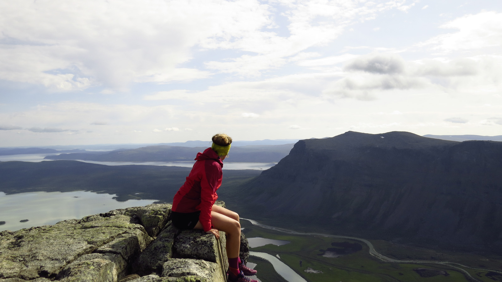 Frau sits on a rocky lead and looks into the distance towards mountains and lakes