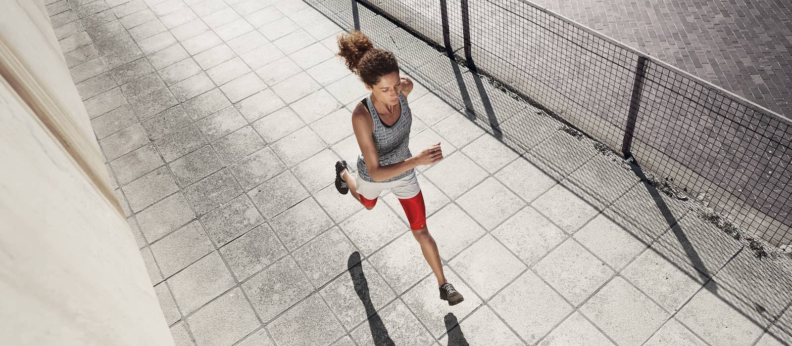 Woman runs over an urban paved surface and wears a red thigh-sleeves