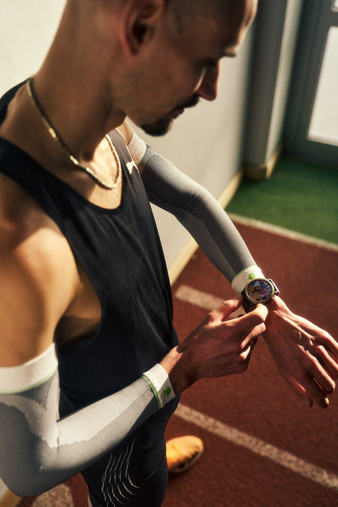 Hendrik Pfeiffer checks his running watch during training on the indoor track, wearing compression arm sleeves for stability and performance.