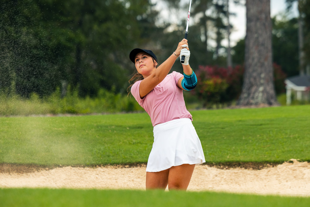 Female golfer playing from a bunker while wearing an elbow support for stability during the golf swing.
