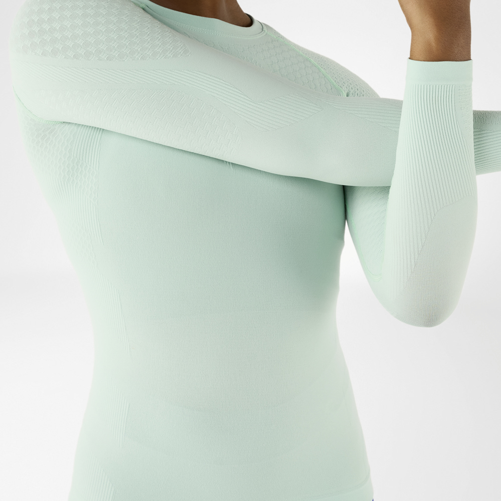 Close-up of a sporty woman in a light green, long-sleeved compression shirt stretching.