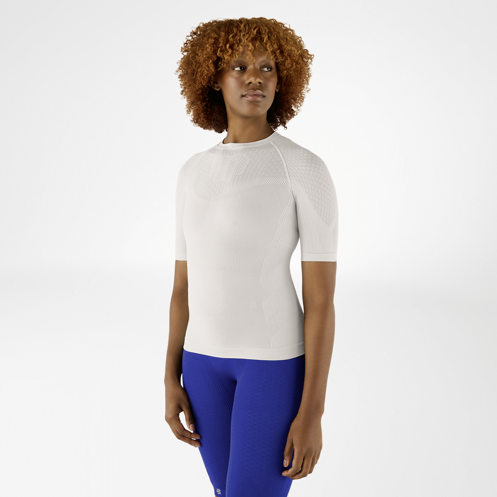 Woman with curly hair in a silver-grey compression shirt and blue leggings. She is standing facing forward and looking to the side.