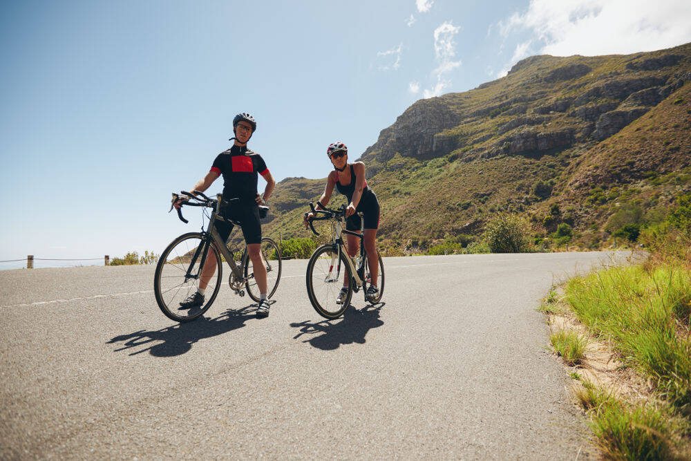 A man and a woman with her racing bikes stand on a street in the mountains