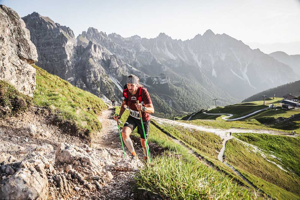 Ultra runner climbing a steep alpine mountain trail with running poles