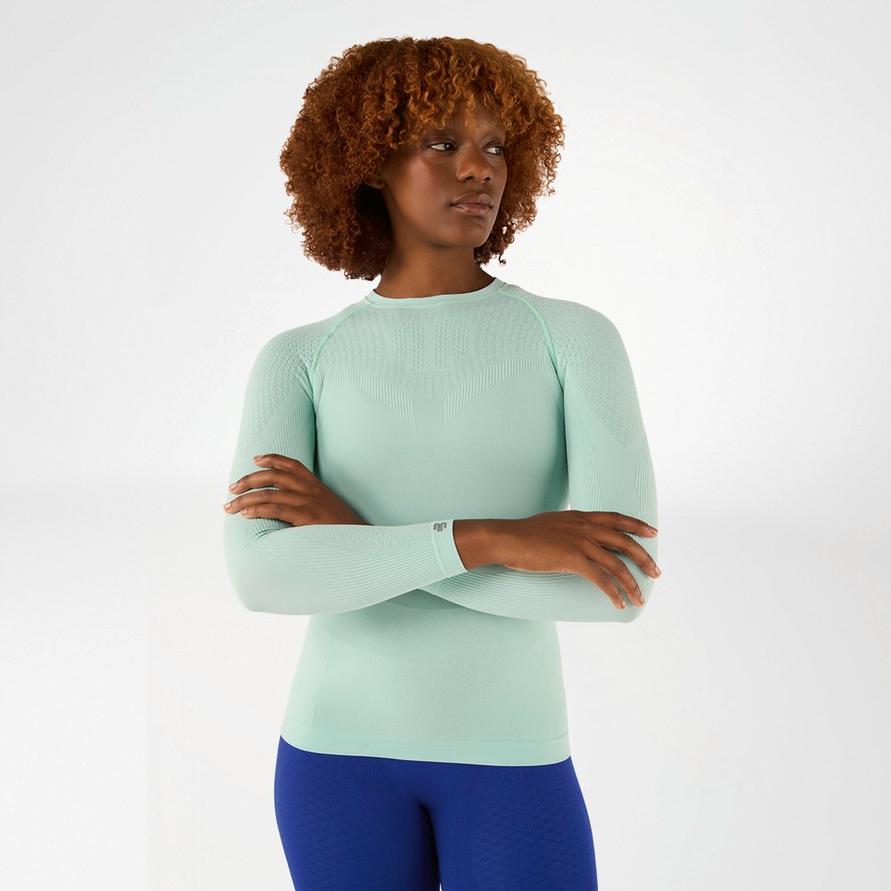 Woman in a light green, close-fitting long sleeve shirt with crossed arms, front view