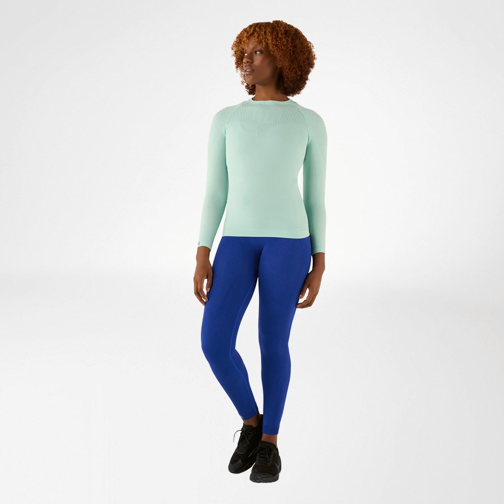 Woman in a mint green, close-fitting long sleeve shirt and blue compression pants, front view
