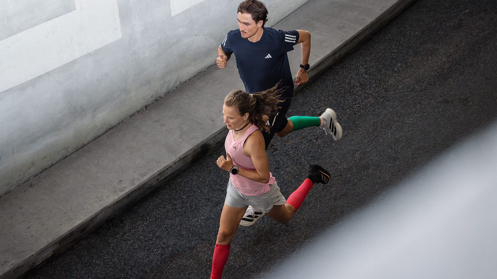 Two women run vigorously through an old town street with small balconies
