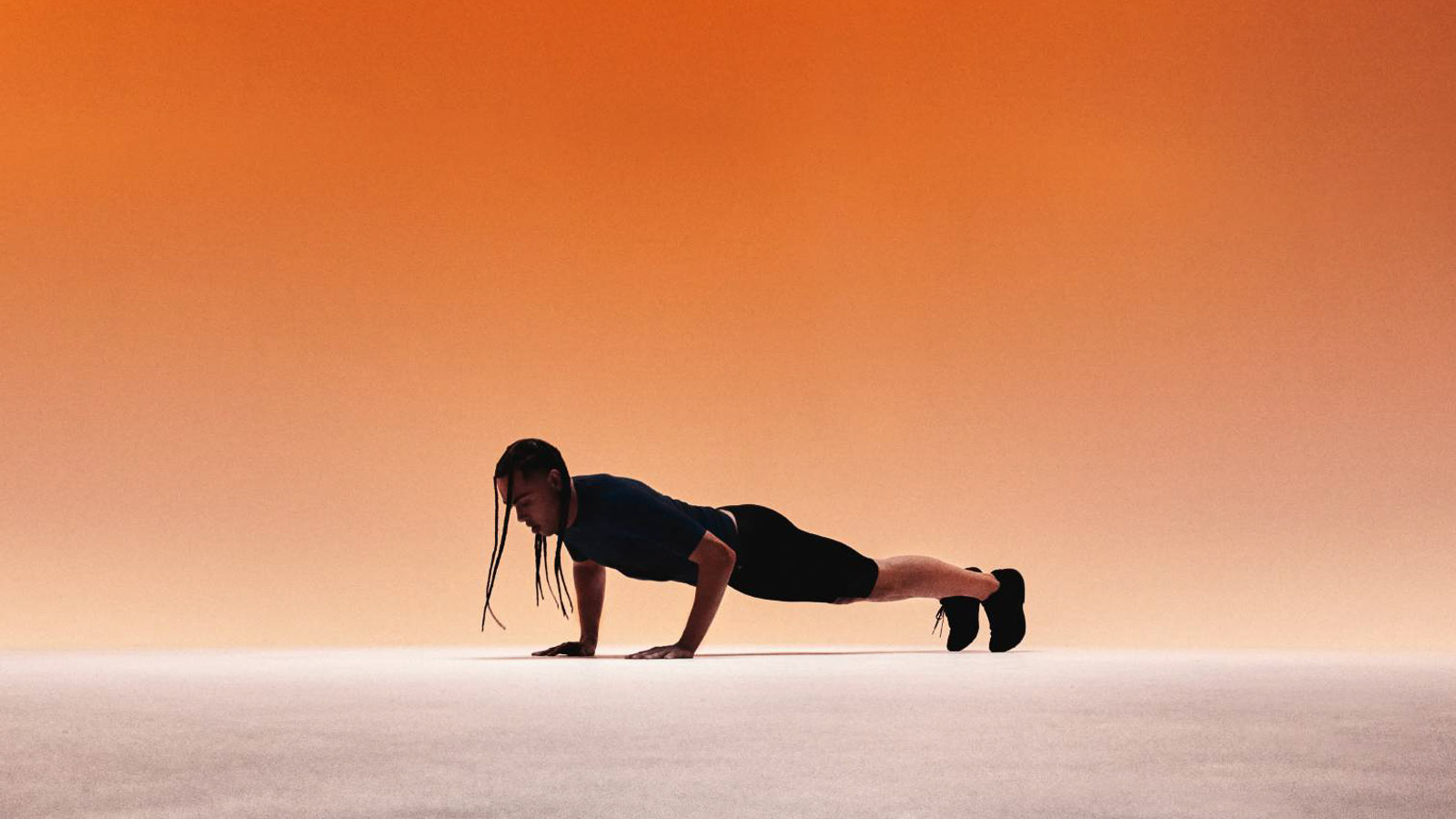 Athlete in blue sportswear with compression shirt and compression pants doing push-ups in front of an orange background.