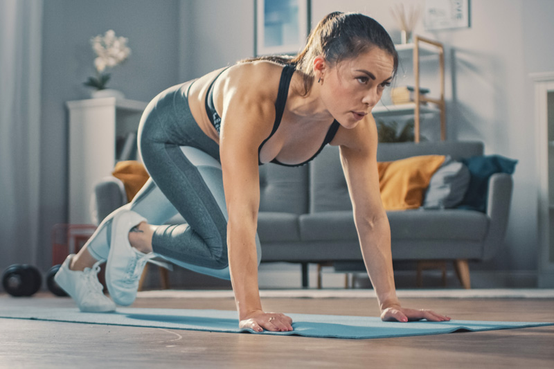 Woman makes Mountain Climbers in the living room in the background a couch and shelves