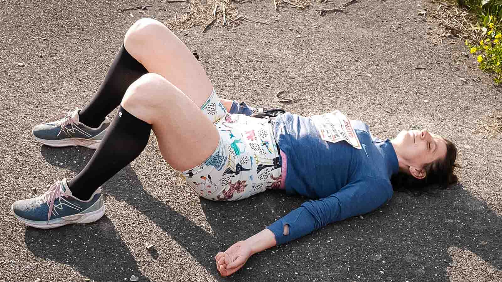 A woman in knee-length socks lies exhausted on the ground with her legs bent after the Rennsteig run