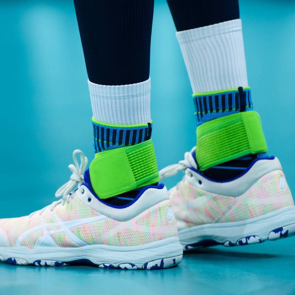 Close-up of a volleyball player’s legs on an indoor court. The Bauerfeind Sports Ankle Support Rivera is worn over high white socks.