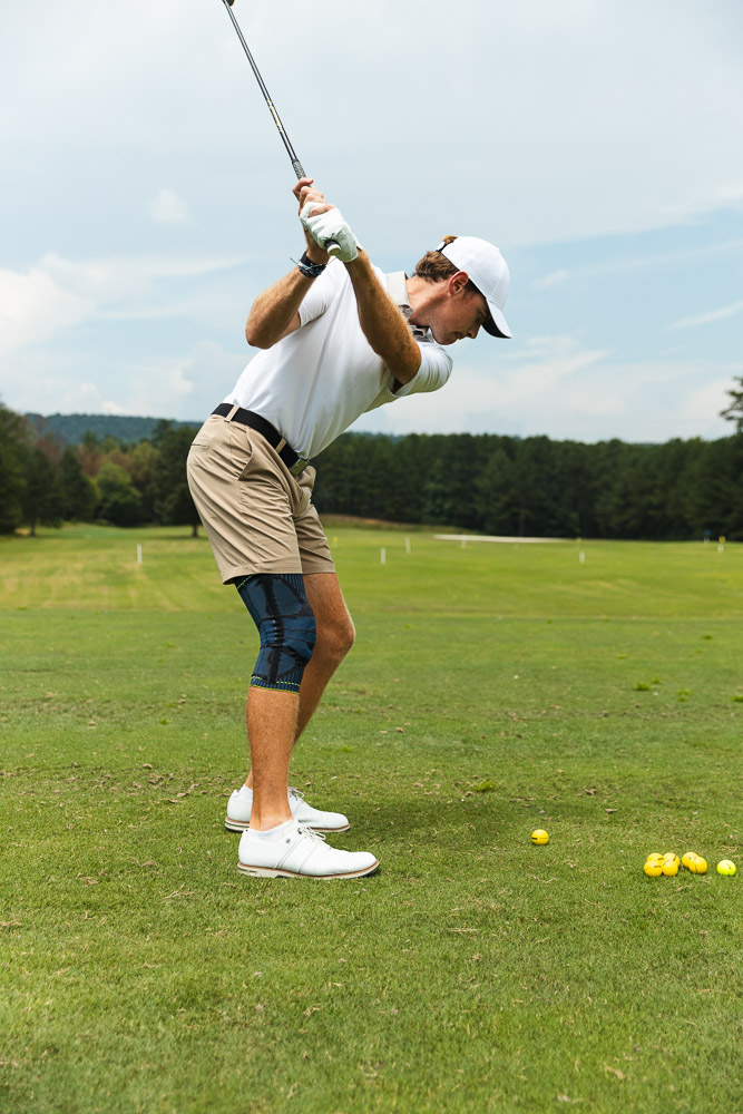 Golfer swinging on the course while wearing a knee brace for stability and support during golf.