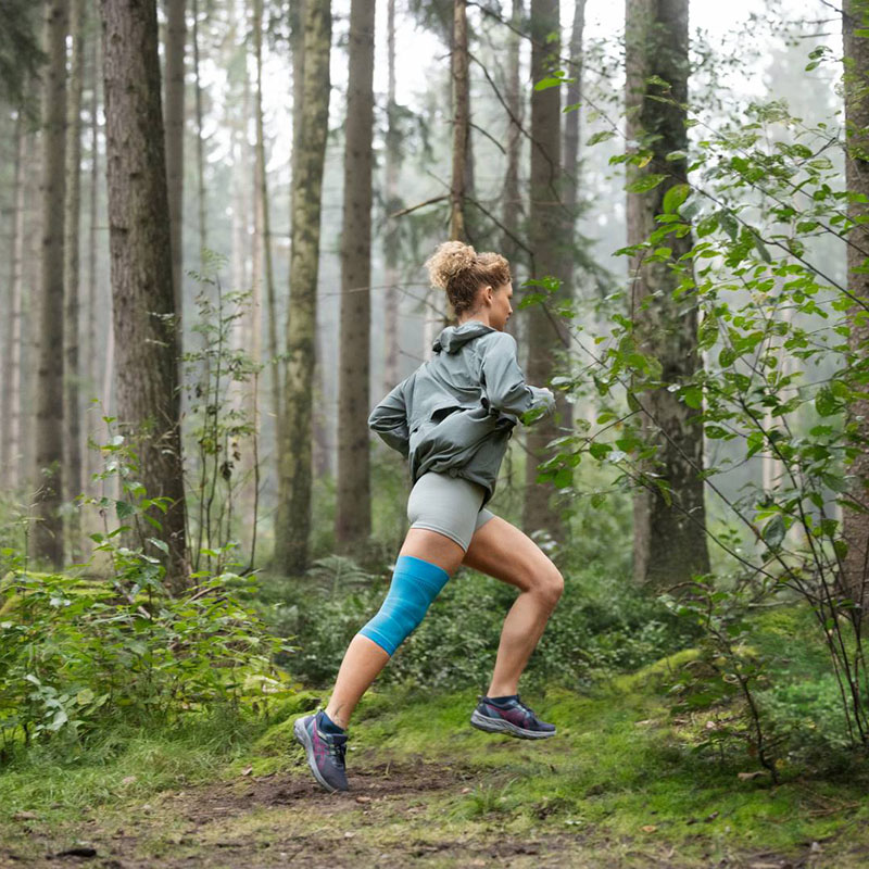 Runner in the forest with a knee bandage A female runner with a knee bandage is running through a dense forest