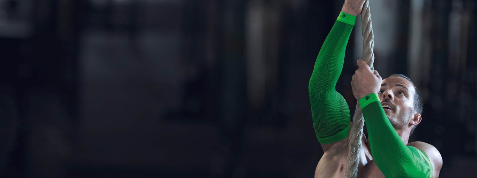 Man with free torso and green arm-sleeves tries to pull up on a rope