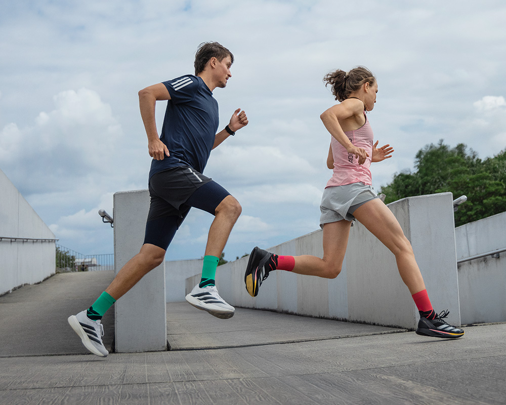 Group of three runners runs around one corner in an old town with graffiti on the walls on a staircase