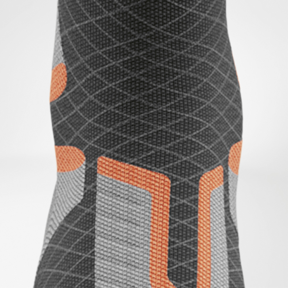 Smart zones. Full control. Detailed view of the shin area with visible functional zones in orange and grey for targeted pressure distribution while skiing.