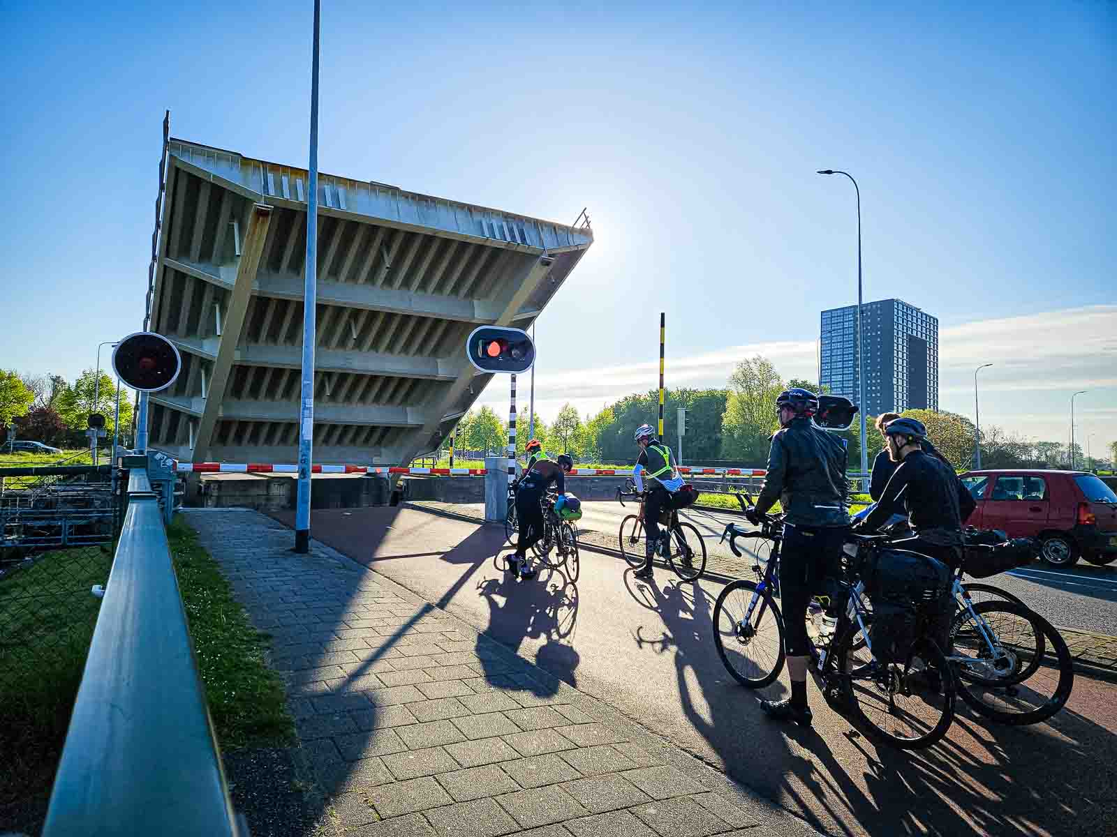 Various participants in the Race around the Netherlands stand waiting by a raised bridge.