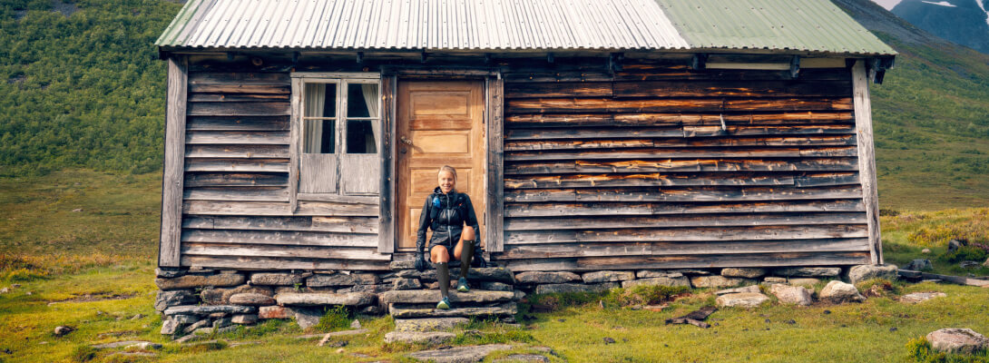 Young woman sits on the steps of a wooden house and smiles into the camera she wears sports socks for regeneration
