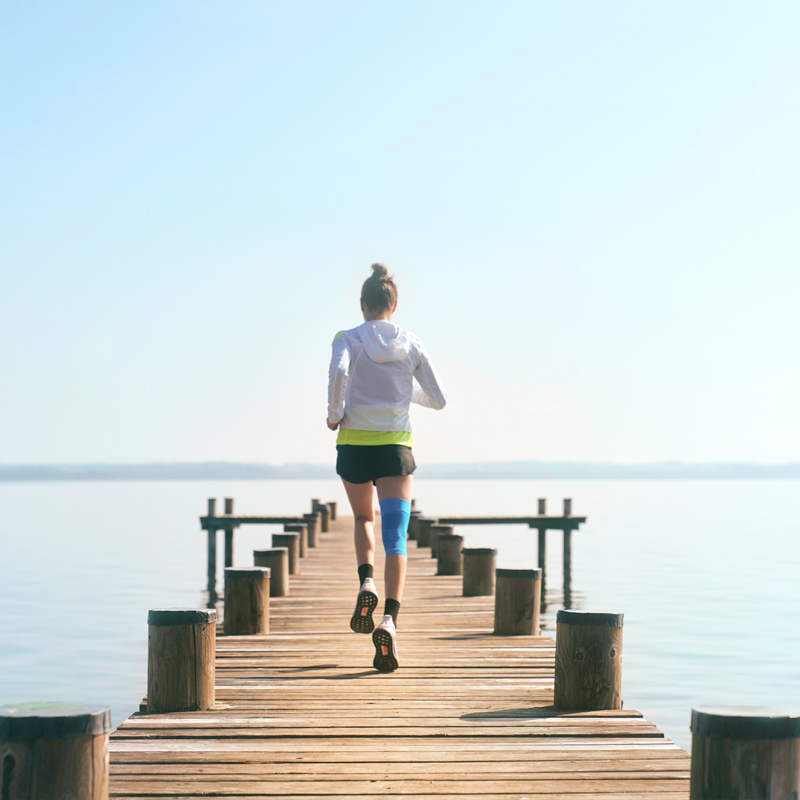Anna Hahner runs with her Sports Compression Knee Support via a jetty towards the lake