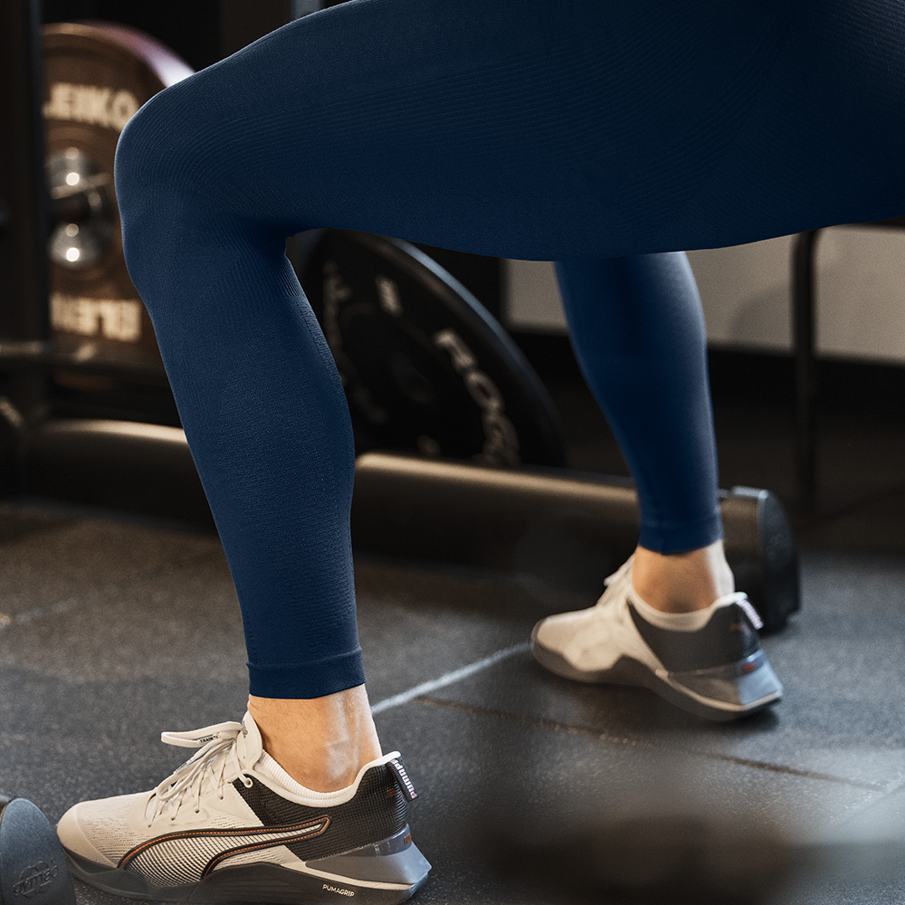 Stability starts at the base – Compression tights for lower body training Close-up of an athlete’s legs in blue compression tights during a workout in the gym. The tight fit enhances stability and blood circulation.