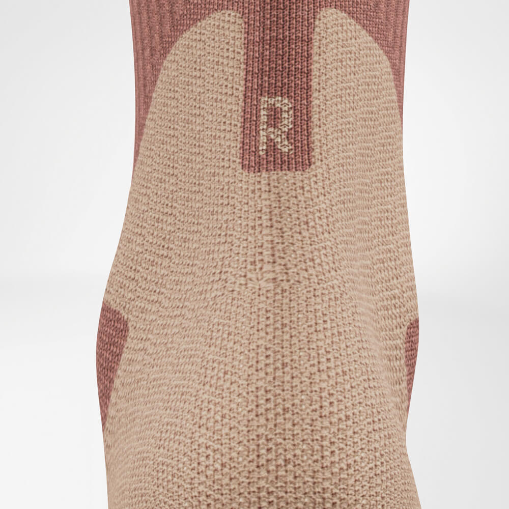 Close-up of the Achilles area of an outdoor sock in coral and gray. The detailed knit structure highlights the comfort zone in the heel area.