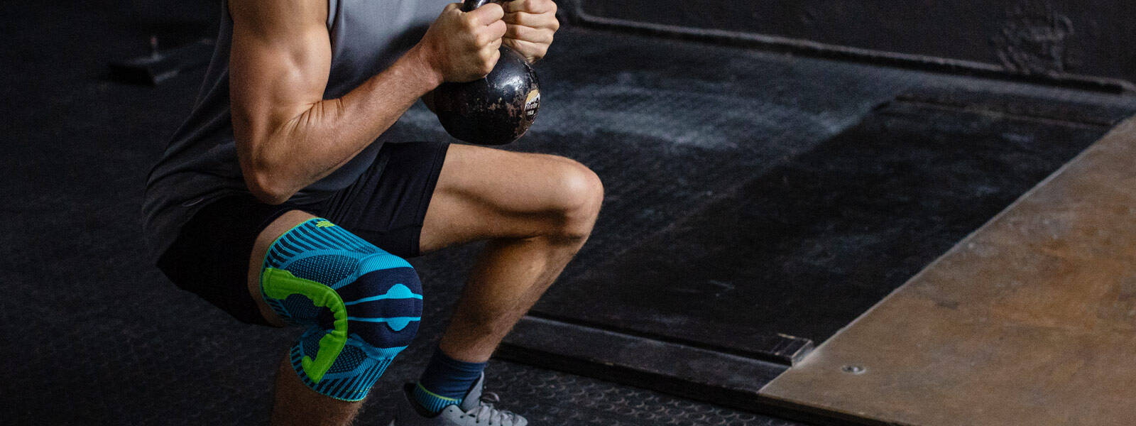 Man with a kneeboard goes deeply crouched with a kettlebell between the two hands