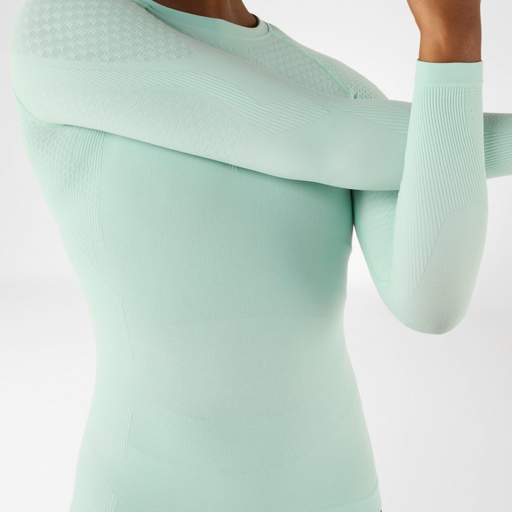 Close-up of a sporty woman in a light green, long-sleeved compression shirt stretching.