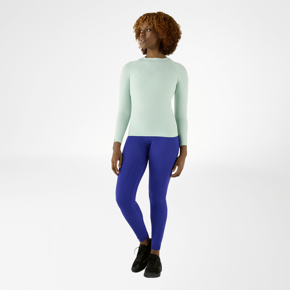 Woman in a mint green, close-fitting long sleeve shirt and blue compression pants, front view