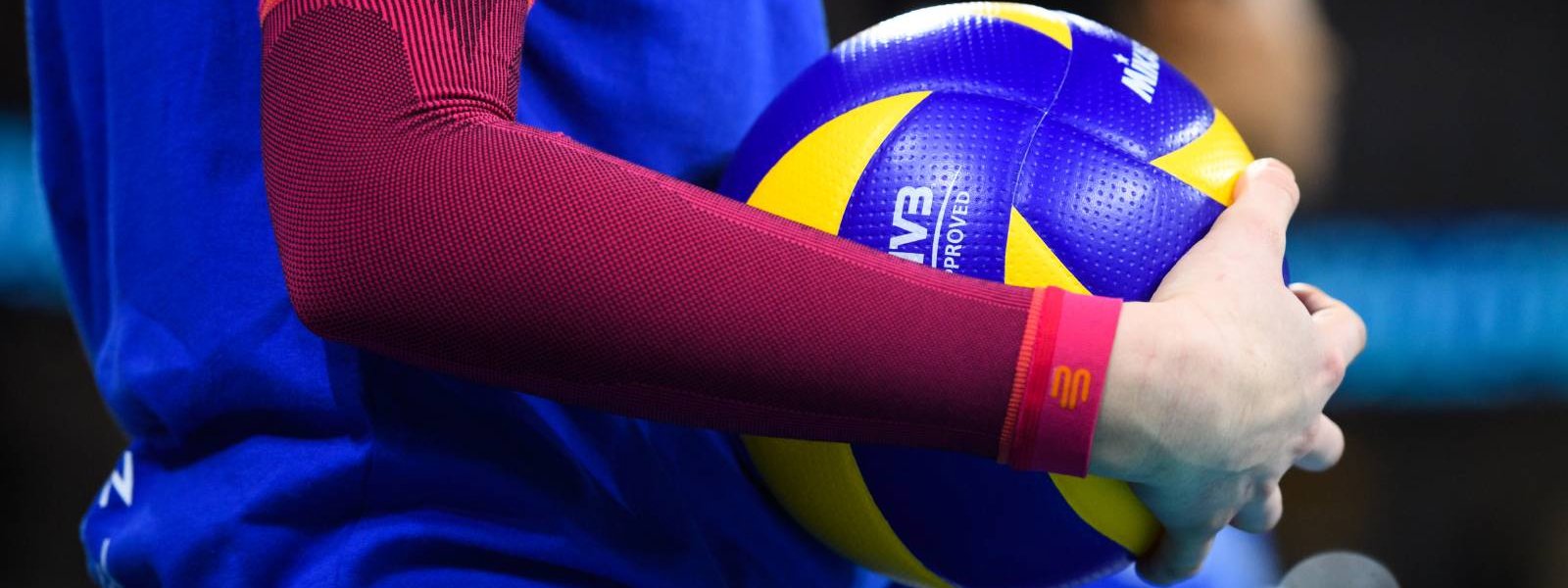 Volleyball player with pink arm sleeves has a volleyball in her hand