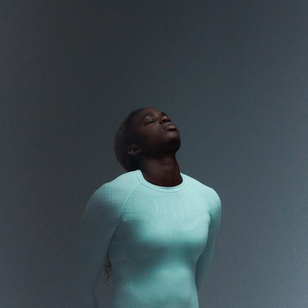 Athlete in mint green sports top wears a plait, has her hands on her hips and was photographed from the side