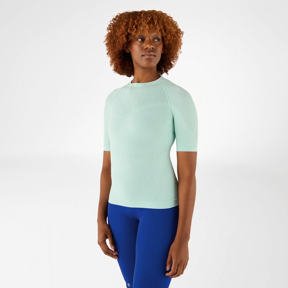 Woman in a mint green compression shirt and blue leggings, standing facing forward.