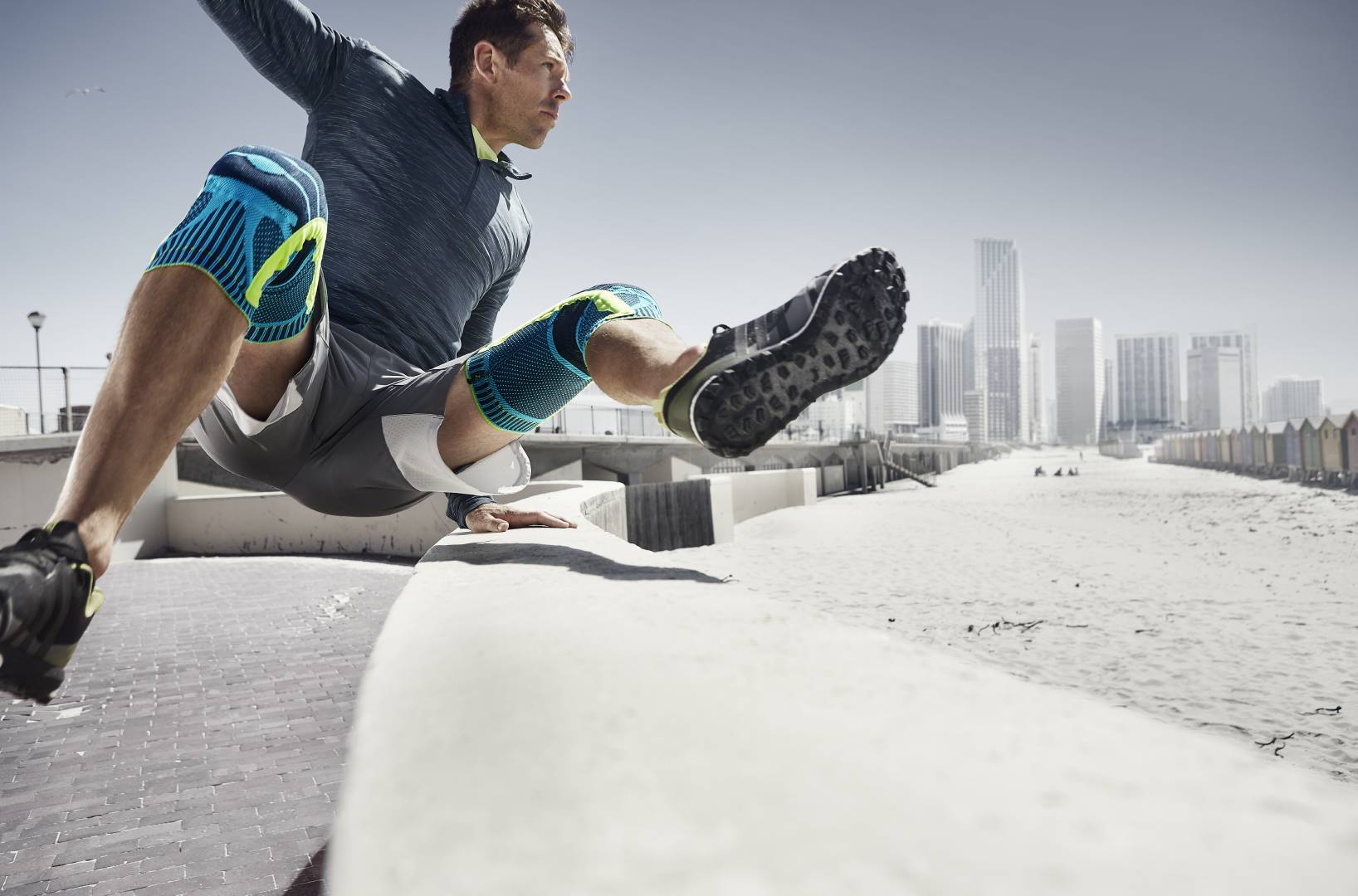 Mann with two knee bands jumps over an obstacle in the background of the Urban Running